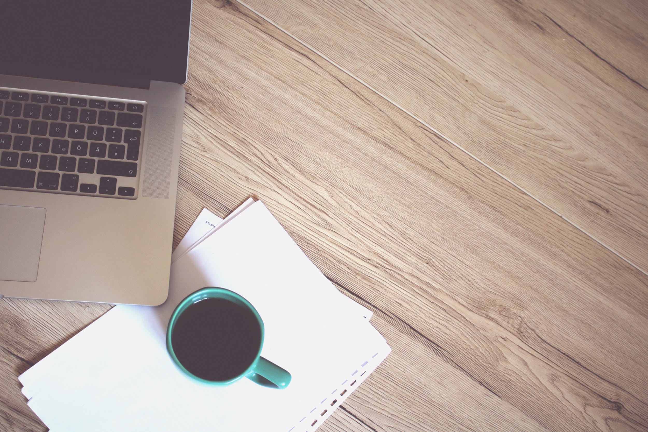 A photo of a laptop, notebook, and coffee cup on a table