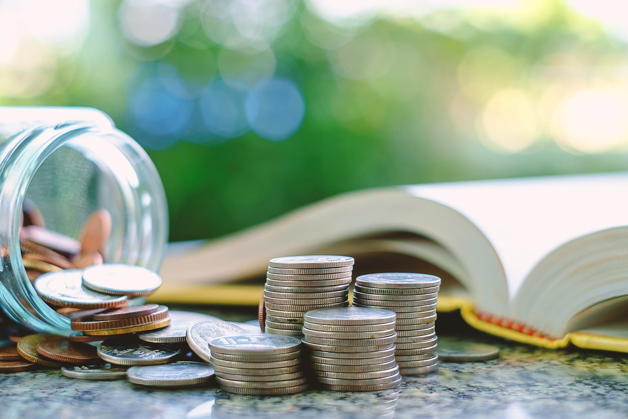 A savings jar on it's side next to stacks of coins